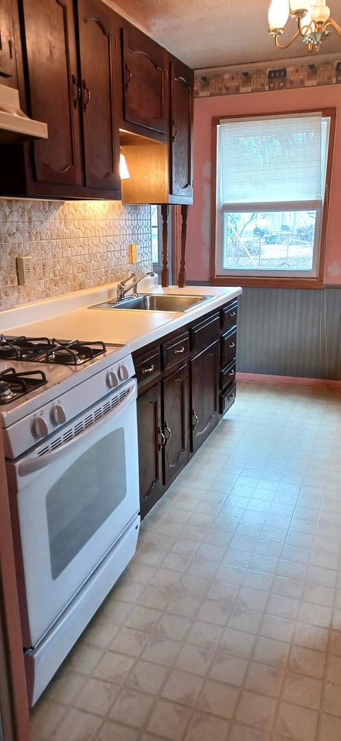 kitchen featuring sink, white gas range oven, dark brown cabinets, and a notable chandelier