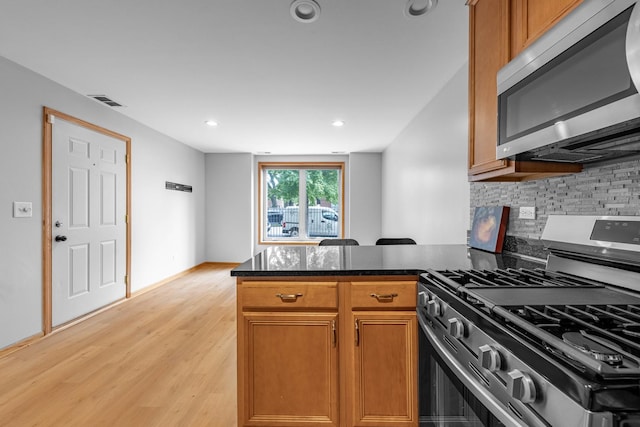 kitchen featuring appliances with stainless steel finishes, decorative backsplash, dark stone counters, kitchen peninsula, and light hardwood / wood-style flooring