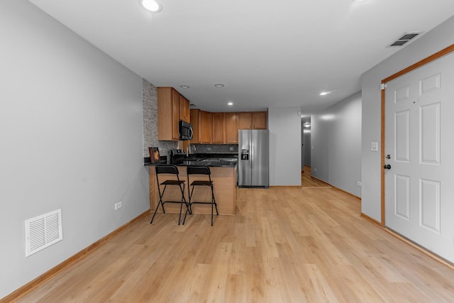 kitchen with appliances with stainless steel finishes, tasteful backsplash, a kitchen bar, kitchen peninsula, and light wood-type flooring