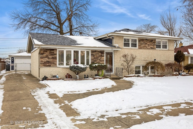 tri-level home with a garage, brick siding, a gate, and an outbuilding