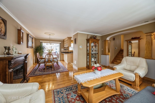 living area featuring arched walkways, light wood finished floors, visible vents, stairway, and ornamental molding