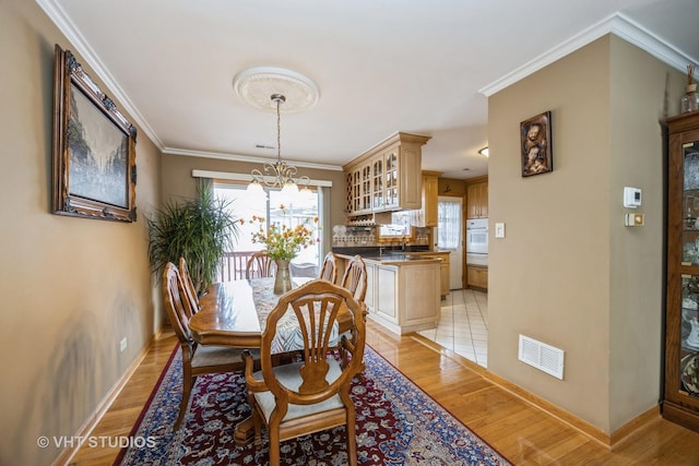 dining space with light wood finished floors, plenty of natural light, visible vents, and ornamental molding