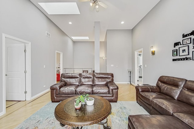 living area with a skylight, visible vents, a high ceiling, light wood-type flooring, and baseboards