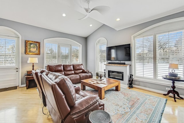 living room featuring lofted ceiling, a glass covered fireplace, a ceiling fan, and a healthy amount of sunlight