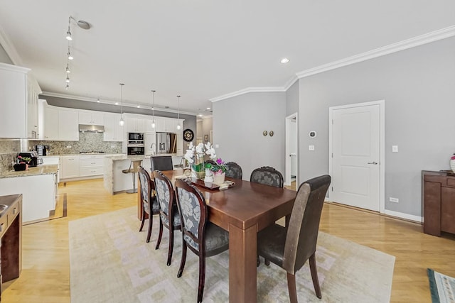 dining room featuring ornamental molding, track lighting, light wood-style flooring, and baseboards