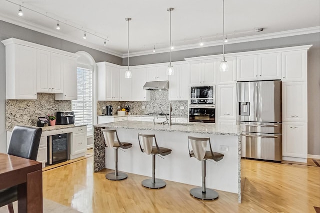 kitchen featuring white cabinets, wine cooler, hanging light fixtures, stainless steel appliances, and under cabinet range hood