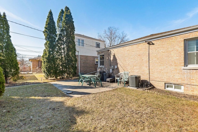 back of property with central air condition unit, brick siding, a lawn, and a patio area