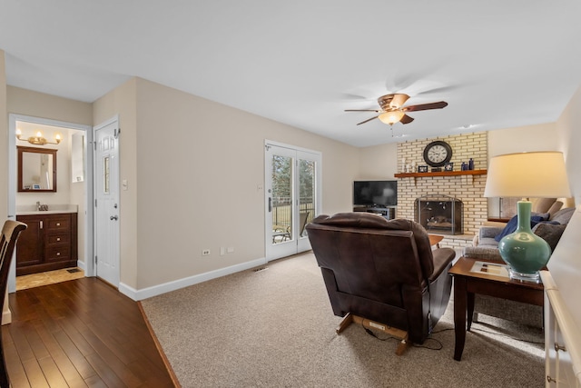 living area featuring dark wood-type flooring, a brick fireplace, a ceiling fan, and baseboards