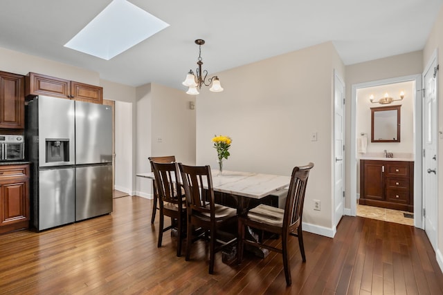 dining space with a chandelier, dark wood-style flooring, a skylight, and baseboards