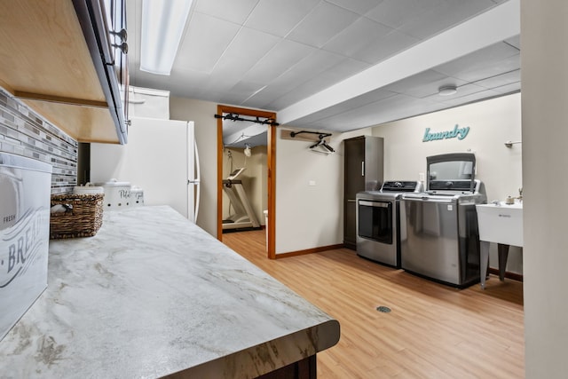 kitchen with washing machine and clothes dryer, light countertops, freestanding refrigerator, light wood-type flooring, and baseboards