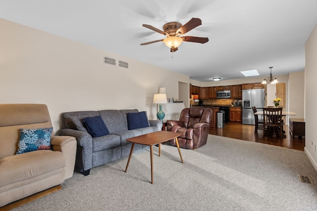 living area featuring ceiling fan with notable chandelier, dark wood finished floors, and visible vents