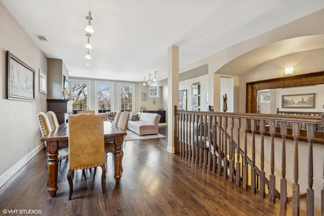 dining room featuring dark wood-style floors, baseboards, visible vents, and arched walkways