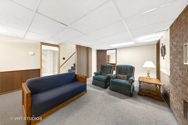 living room featuring stairs, a drop ceiling, a wainscoted wall, and carpet flooring