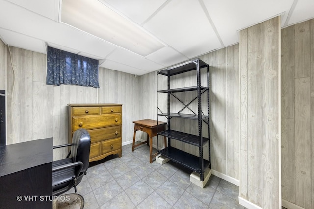 interior space featuring a drop ceiling, baseboards, and wood walls