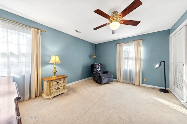 living area with visible vents, baseboards, light colored carpet, and a ceiling fan