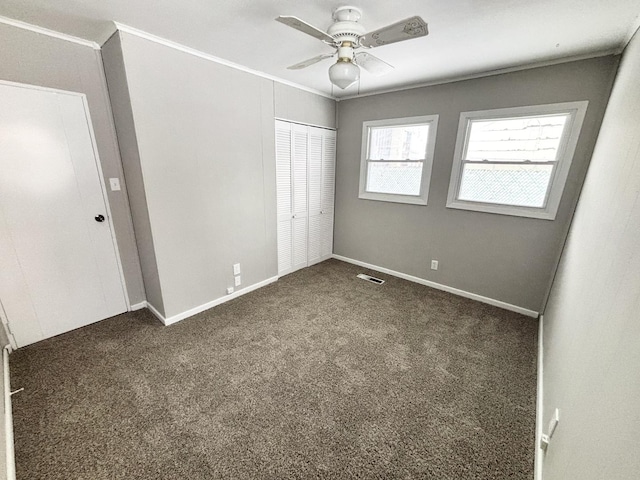 unfurnished bedroom with ceiling fan, ornamental molding, dark carpet, and a closet