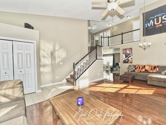 living room featuring a towering ceiling, ceiling fan with notable chandelier, and light wood-type flooring