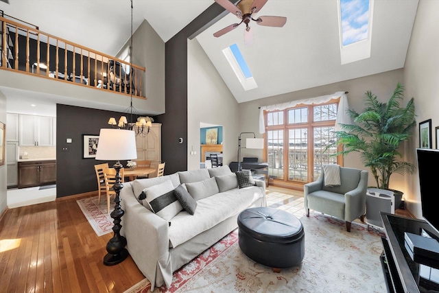 living room with hardwood / wood-style floors, high vaulted ceiling, ceiling fan with notable chandelier, and a skylight