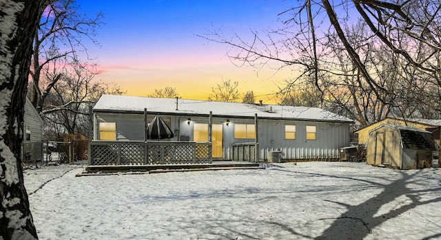 snow covered house with central AC unit and a storage unit