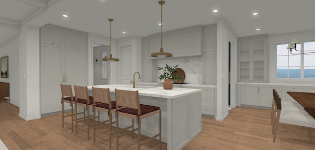 kitchen featuring pendant lighting, tasteful backsplash, a kitchen breakfast bar, a kitchen island with sink, and light wood-type flooring