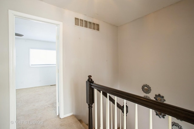 hallway with light carpet, an upstairs landing, and visible vents