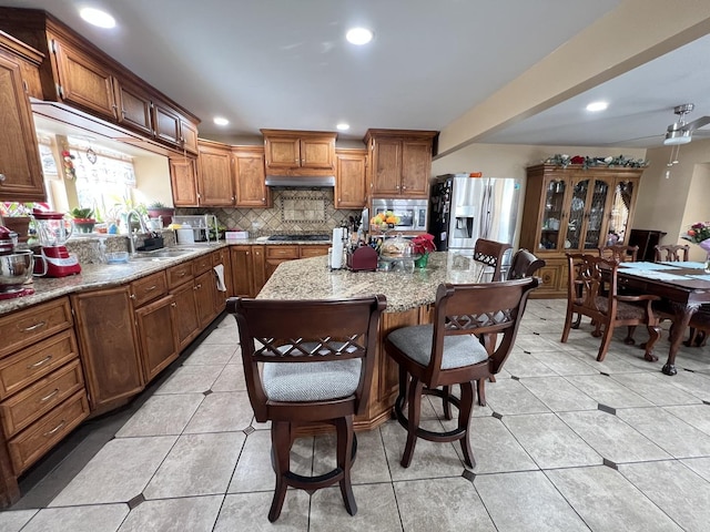 kitchen featuring sink, light stone counters, tasteful backsplash, appliances with stainless steel finishes, and a kitchen island