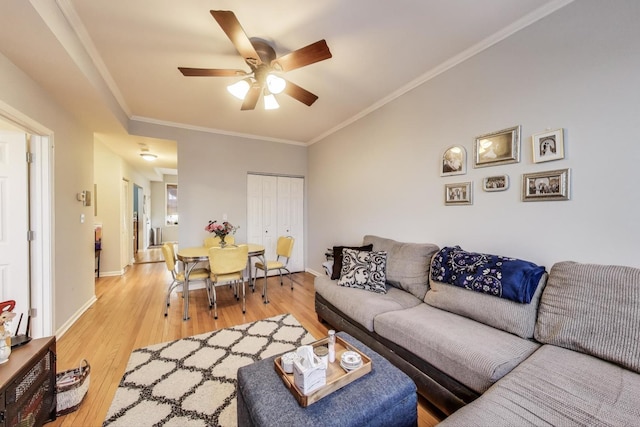 living area featuring light wood-style floors, crown molding, baseboards, and a ceiling fan