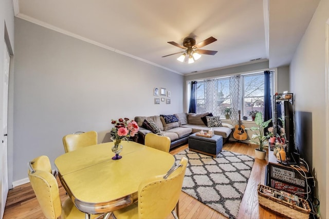 living room featuring crown molding, ceiling fan, visible vents, and light wood-style floors