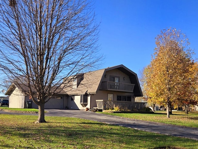 view of front of home with a balcony, a front yard, aphalt driveway, and a gambrel roof