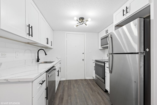 kitchen with sink, appliances with stainless steel finishes, white cabinetry, light stone counters, and dark hardwood / wood-style flooring