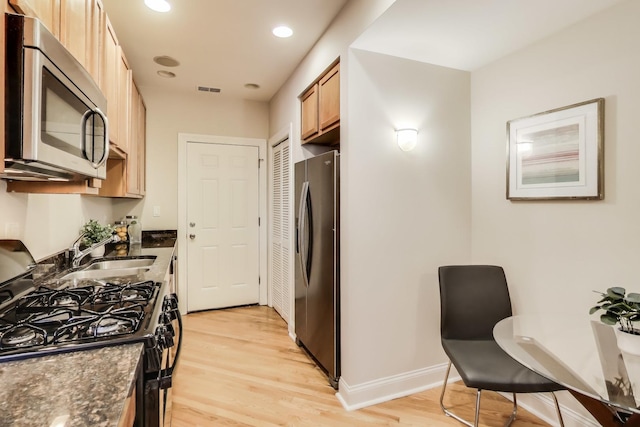 kitchen with dark stone counters, appliances with stainless steel finishes, light wood-type flooring, and a sink