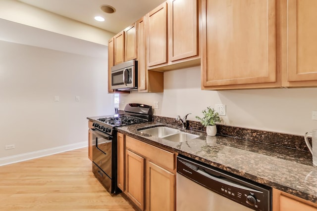 kitchen with stainless steel appliances, a sink, light wood-style floors, baseboards, and dark stone countertops