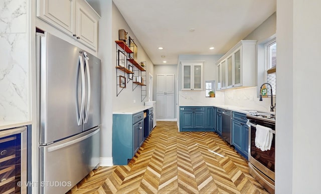 kitchen featuring beverage cooler, tasteful backsplash, appliances with stainless steel finishes, blue cabinets, and a sink