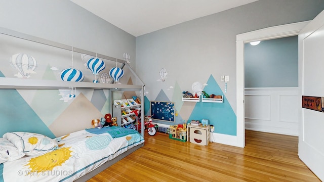 bedroom featuring wainscoting, a decorative wall, and wood finished floors