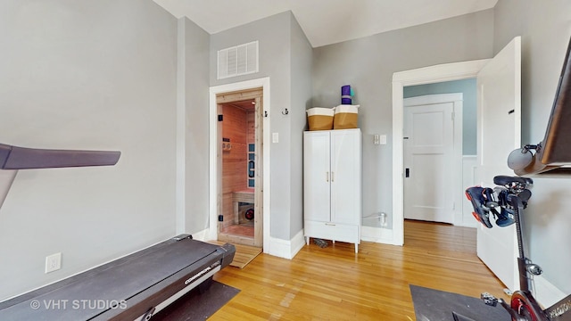 workout area featuring light wood finished floors, baseboards, and visible vents