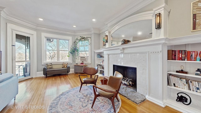 living area with a fireplace with raised hearth, crown molding, radiator heating unit, and wood finished floors