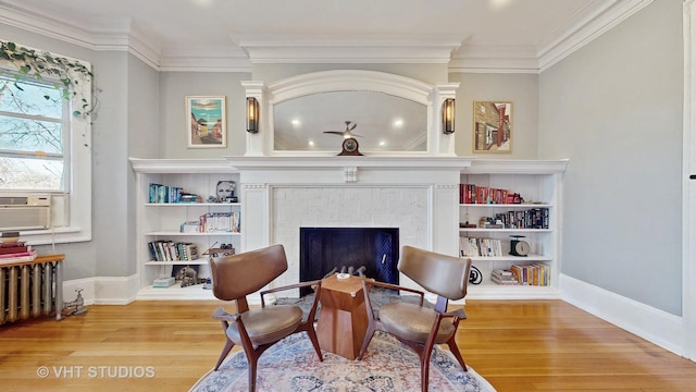 living area featuring radiator heating unit, a fireplace, wood finished floors, and crown molding