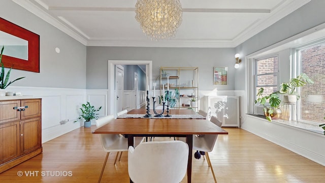 dining room with light wood-style floors, a chandelier, a wainscoted wall, and ornamental molding