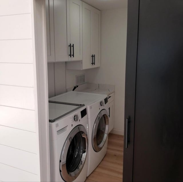 clothes washing area with cabinets, washer and clothes dryer, and light hardwood / wood-style floors