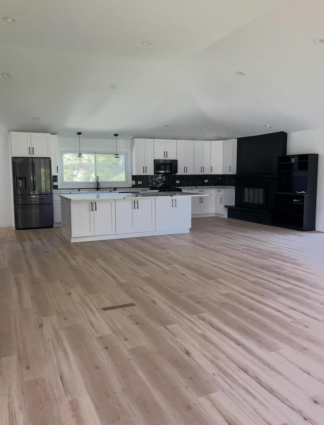 kitchen featuring white cabinetry, black fridge with ice dispenser, hanging light fixtures, and a kitchen island