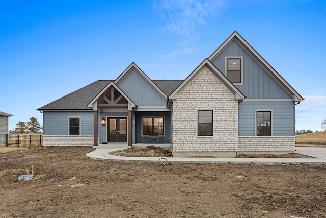 view of front facade with board and batten siding, french doors, fence, and stone siding