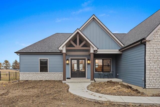 view of front facade featuring roof with shingles, fence, board and batten siding, and french doors