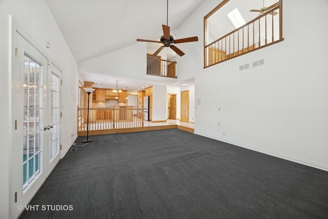 unfurnished living room with ceiling fan, a skylight, high vaulted ceiling, dark colored carpet, and french doors