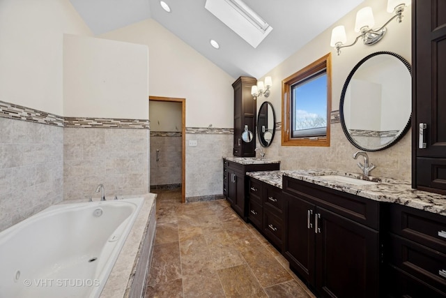 bathroom featuring vanity, vaulted ceiling with skylight, tile walls, and tiled tub