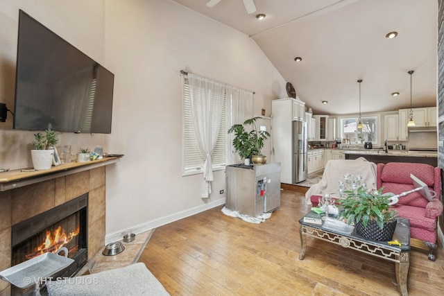 living room featuring vaulted ceiling, ceiling fan, light hardwood / wood-style flooring, and a fireplace