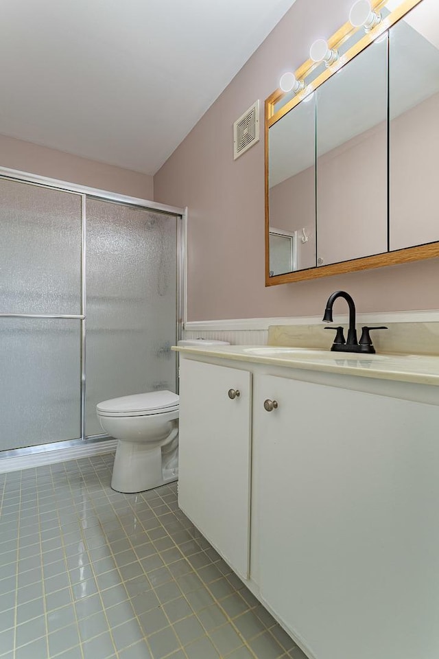 bathroom with a shower with door, vanity, tile patterned floors, and toilet