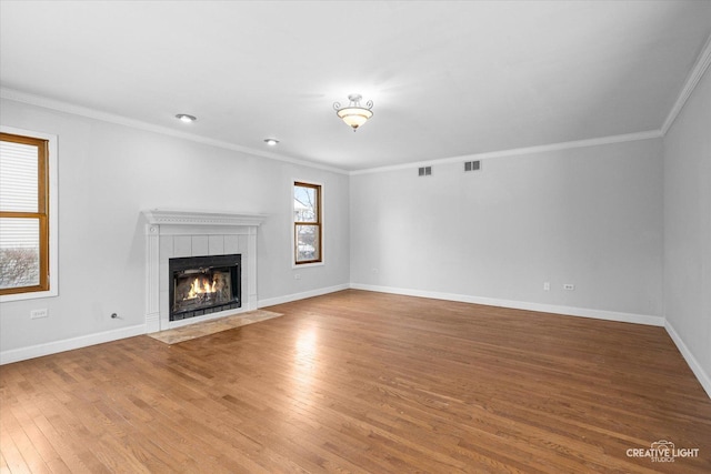 unfurnished living room featuring a tile fireplace, ornamental molding, and hardwood / wood-style floors