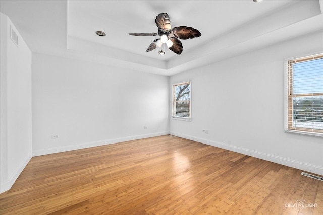 spare room with light hardwood / wood-style flooring, a raised ceiling, and ceiling fan