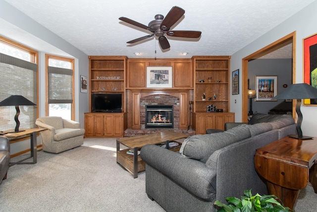 living area with a textured ceiling, ceiling fan, a fireplace, and light carpet