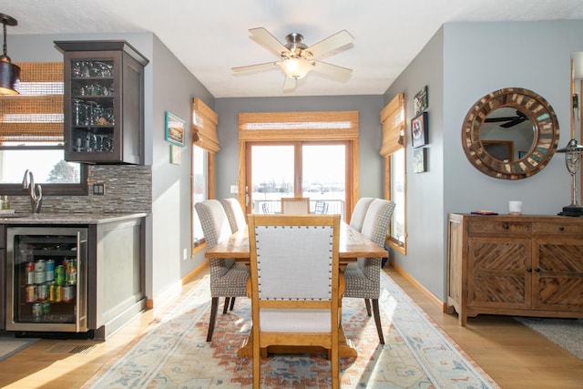 dining area featuring wet bar, light wood-style flooring, beverage cooler, and a healthy amount of sunlight